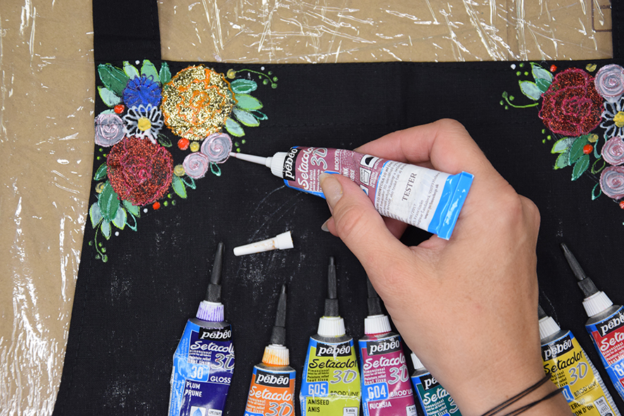Žena maľuje detaily kvetov, lístkov, budky a vetvičky pomocou kontúr na textil.